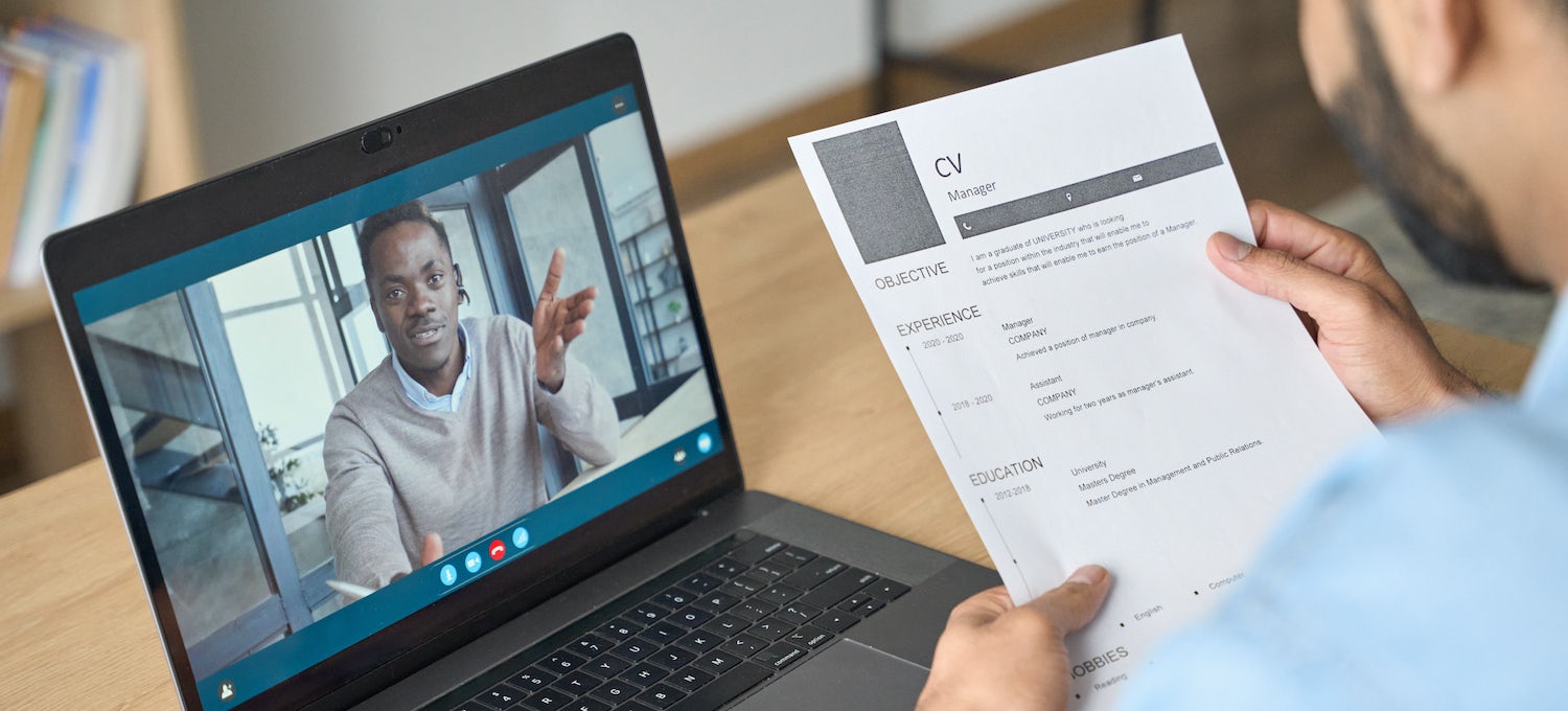 [Featured image] An infographic cover letter sits in the foreground, held by an interviewer. In the background, a man appears on a laptop screen in a Zoom interview.