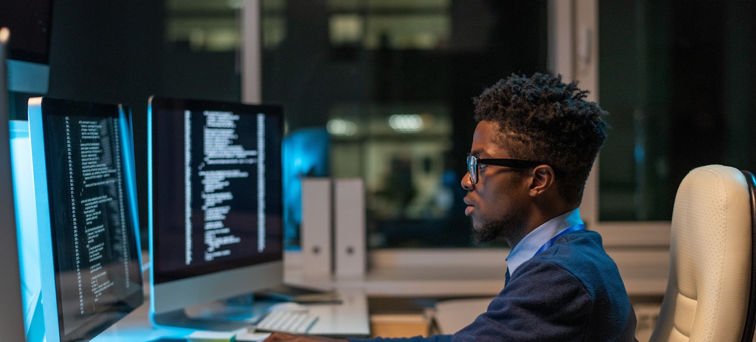 [Imagen destacada] Un hombre con jersey azul y gafas recopila y analiza datos sentado frente a su computadora. 