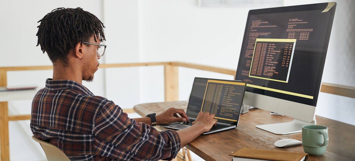 [Featured image] An ethical hacker in a plaid shirt and glasses competes to win a bug bounty on a laptop computer while sitting at a desk with a large desktop monitor.
