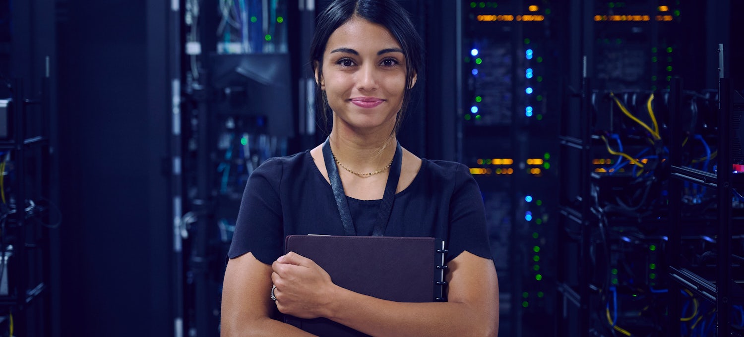 [Featured image] A cybersecurity analyst holds a notebook and stands in front of a room filled with servers.