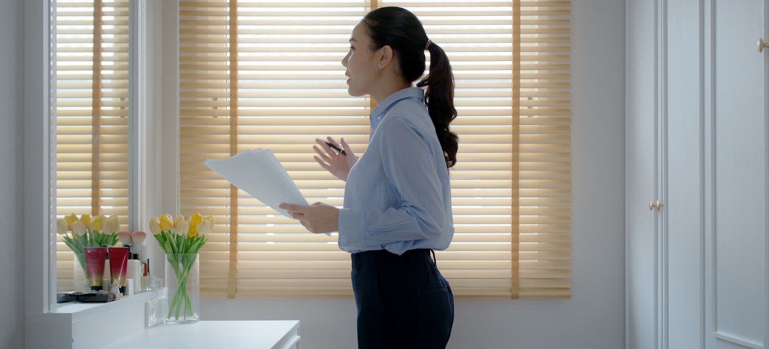 [Featured image] A woman in business attire practices for an interview in front of a mirror.